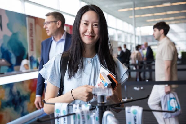 Smiling woman at SIIM Annual Meeting holding conference materials in a busy exhibition hall.
