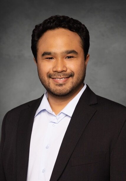 Professional portrait of Theo Dapamede, MD, PhD, attending the SIIM Annual Meeting, showcasing a healthcare expert in a formal suit.