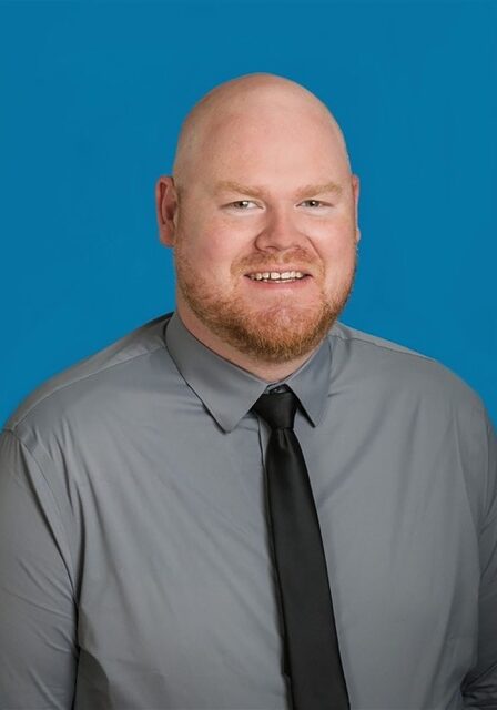 Portrait of Mark Jones at the SIIM Annual Meeting, showcasing a professional individual in a gray shirt and black tie against a blue background.