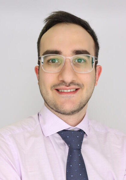 Generated ALT tag: Professional male attendee at the SIIM Annual Meeting, wearing glasses and a light purple shirt with a dark tie, smiling against a plain background.