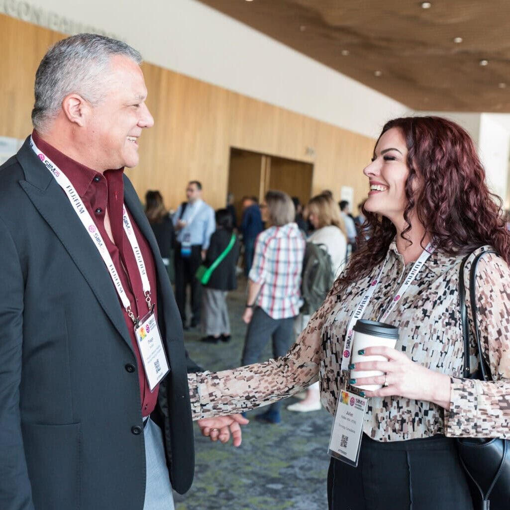 1. Two conference attendees smiling and shaking hands at the SIIM Annual Meeting, networking during medical imaging and health informatics event.