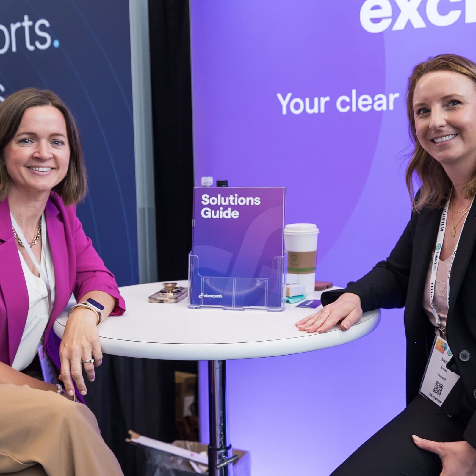 Two women smiling and sitting at a round table during the SIIM Annual Meeting, engaging in a professional discussion.