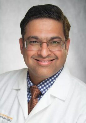 Highly detailed image of a smiling male medical professional wearing a white coat and glasses, attending the SIIM Annual Meeting focused on medical imaging innovation and networking opportunities.