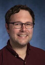 A person smiling in professional attire, wearing glasses, at the SIIM Annual Meeting, a key event for medical imaging and informatics professionals.